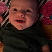 Kasper is registered to the contest to win money with this photo: baby, smiling, infant, face, clothing, blanket, floral_pattern, striped_pattern, lying_down, happy, cute, child, indoors, portrait, skin, hand, head, toddler, dark_green, fabric