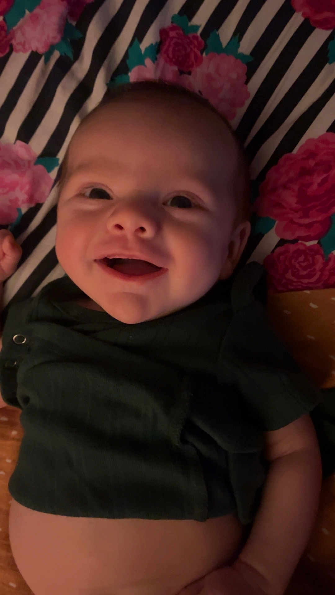 Kasper is registered to the contest to win money with this photo: baby, smiling, infant, face, clothing, blanket, floral_pattern, striped_pattern, lying_down, happy, cute, child, indoors, portrait, skin, hand, head, toddler, dark_green, fabric