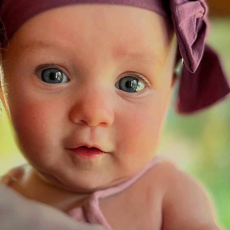 Parker is registered to the contest to win money with this photo: adorable, baby, bow, child, close_up, curious, cute, expression, eyes, face, headband, headwear, indoor, infant, person, portrait, purple, skin, soft_light, young