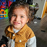 Brentley is registered to the contest to win money with this photo: child, smiling, indoor, playroom, toy, television, hazel_eyes, jacket, brown_hair, buttoned_clothing, floor, wooden_floor, furniture, colorful, happy, portrait, young_child, person, casual_clothing, playtime