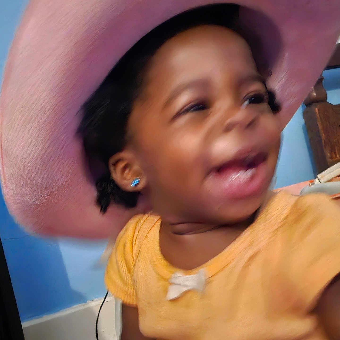 Jamilla is registered to the contest to win money with this photo: baby, child, clothing, cute, ear, earrings, face, happy, hat, indoor, joyful, motion_blur, person, pink_hat, playful, portrait, smiling, toddler, yellow_shirt, young_child