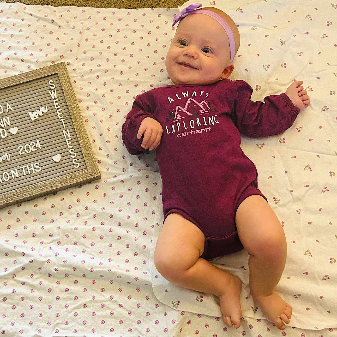 Matilda is registered to the contest to win money with this photo: baby, bodypart, clothing, cushion, dress, face, finger, furniture, hand, head, homedecor, person, photography, portrait, purple, quilt, sitting, t_shirt, text, toy