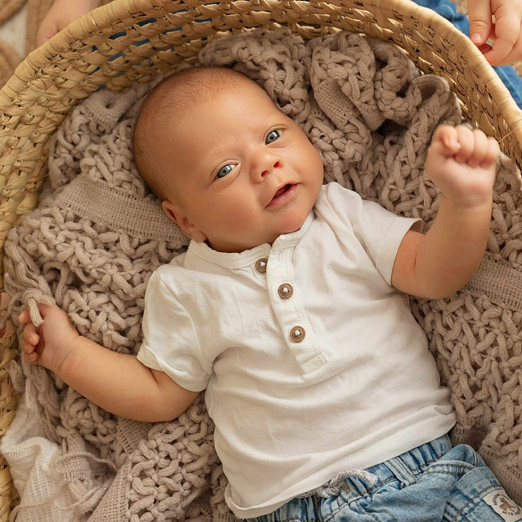 Emylio participe au concours pour gagner de l'argent avec cette photo : baby, basket, blanket, blue_eyes, child, cozy, cute, denim_shorts, face, hands, infant, knit, person, portrait, raised_arm, skin, smiling, texture, white_shirt, woven