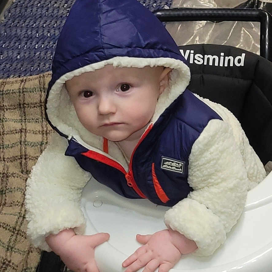 Trentin joined the competition — help win amazing prizes! baby, baby_walker, blanket, child, cozy, curious, cute, face, hands, hooded_jacket, indoor, infant, looking_up, person, plush, rug, seated, soft_fabric, walker, warm_clothing