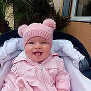 Camille a rejoint le concours — aidez-le/la à gagner de superbes lots ! baby, child, pink_hat, pink_jacket, stroller, smiling, tongue_out, outdoor, plants, greenery, window, building_wall, cute, happy, infant, portrait, cold_weather, baby_clothing, person, face