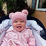 baby, child, pink_hat, pink_jacket, stroller, smiling, tongue_out, outdoor, plants, greenery, window, building_wall, cute, happy, infant, portrait, cold_weather, baby_clothing, person, face