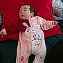 baby, infant, onesie, red_pillow, lying_down, sleepy, cute, soft_fabric, child, indoor, face, hand, footed_pajamas, bunny_design, text_on_clothing, blanket, comfort, resting, person, toddler