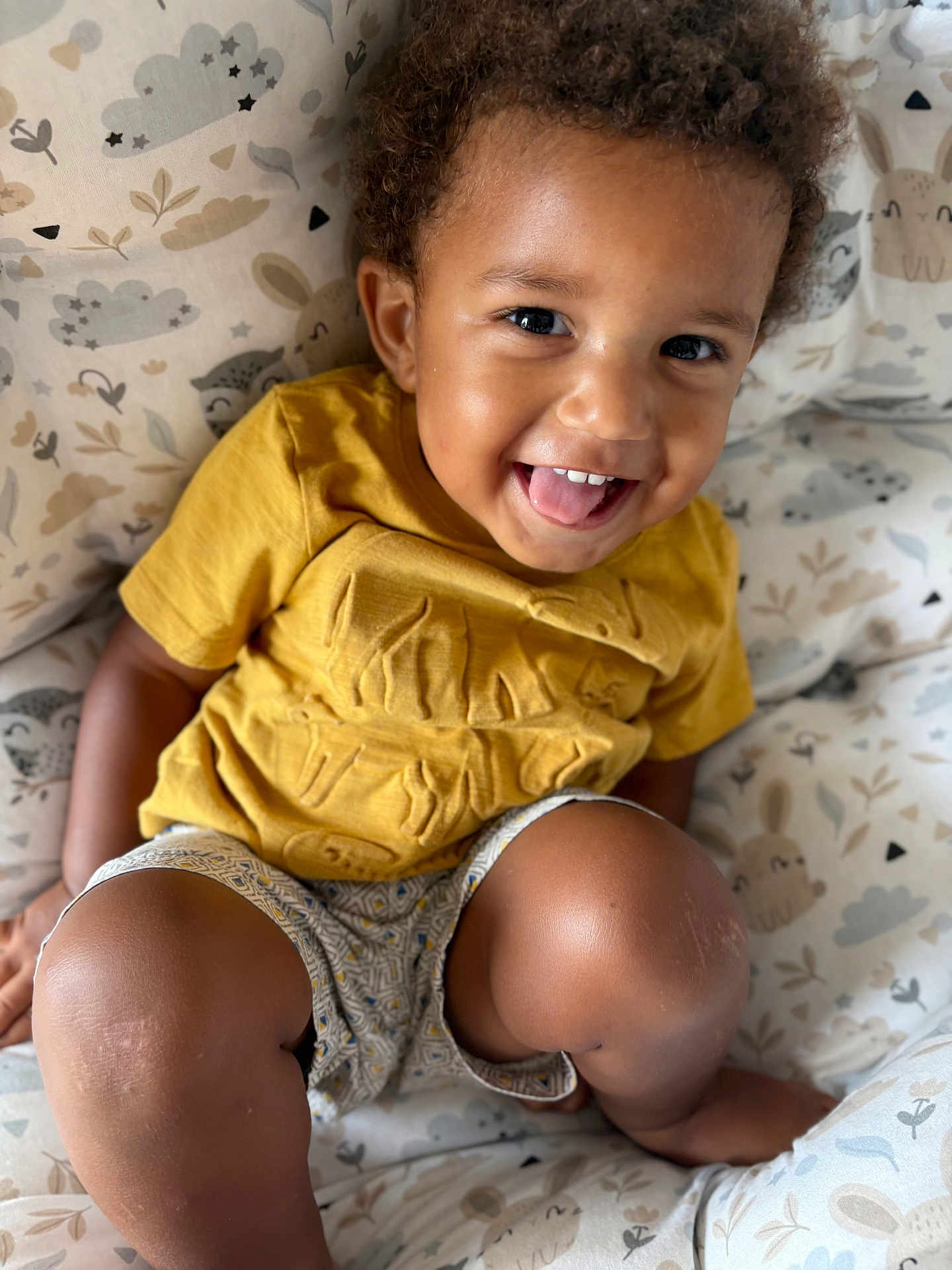 Habib a rejoint le concours — aidez-le/la à gagner de superbes lots ! toddler, child, smiling, happy, face, curly_hair, yellow_shirt, shorts, patterned_clothing, cushion, animal_print, cloud_print, indoor, seated, cute, skin, legs, playful, portrait, baby
