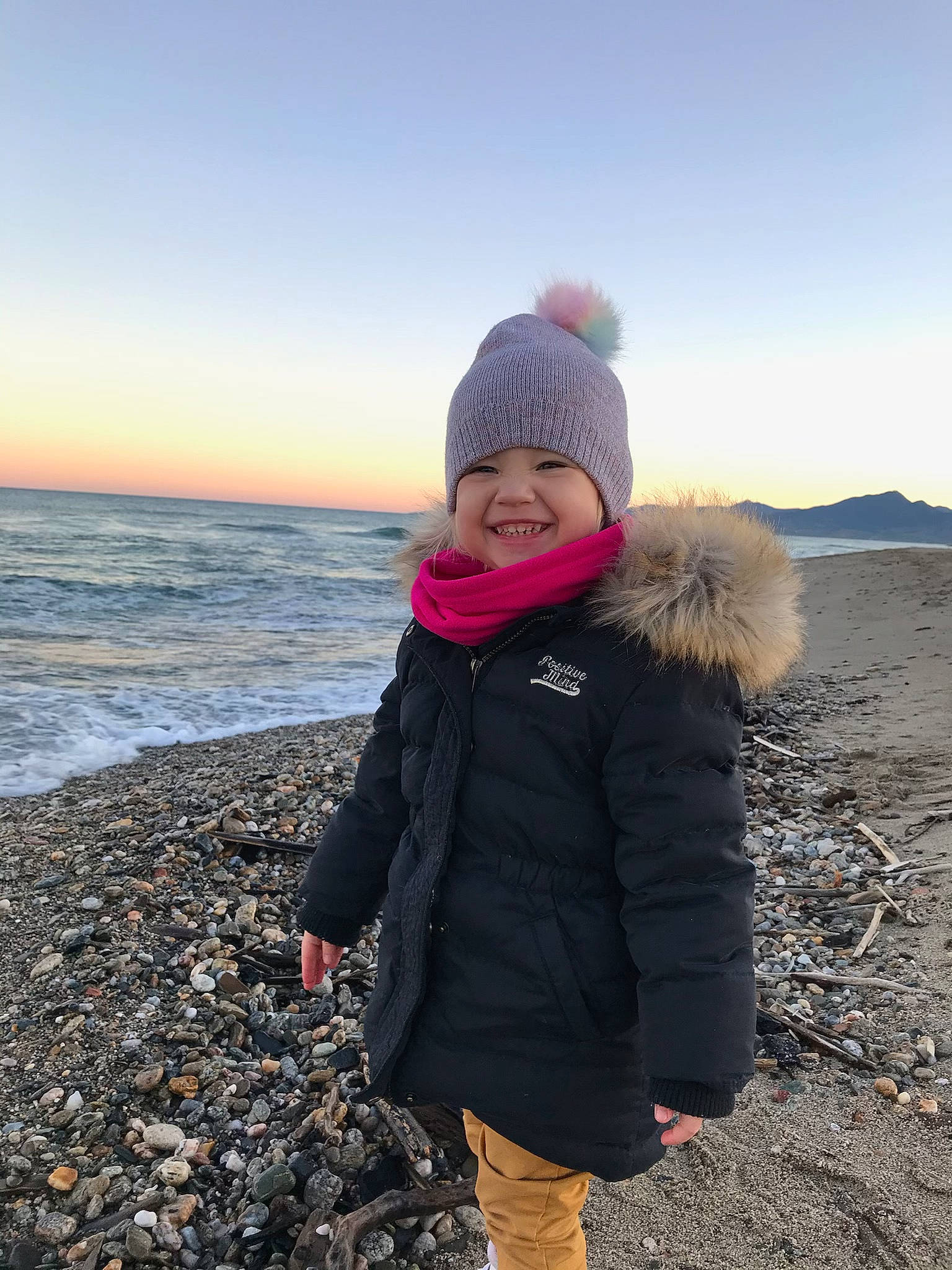 Lily participe au concours pour gagner de l'argent avec cette photo : beach, child, freezing, fun, glove, happy, headwear, jacket, joy, landscape, leisure, outerwear, people_in_nature, person, rock, sky, smile, standing, sunrise, toddler