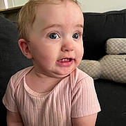 Paisley joined the competition — help win amazing prizes! baby, child, infant, person, face, pink_shirt, ribbed_clothing, couch, cushion, indoor, curious_expression, blue_eyes, short_hair, seated, soft_lighting, closeup, skin, mouth, ear, cheek