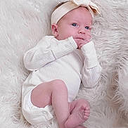 Madelynn joined the competition — help win amazing prizes! baby, infant, newborn, white_clothing, headband, bow, blue_eyes, hand, foot, fingers, lying_down, fluffy_rug, soft_texture, cute, portrait, indoors, cozy, sleepwear, child, person