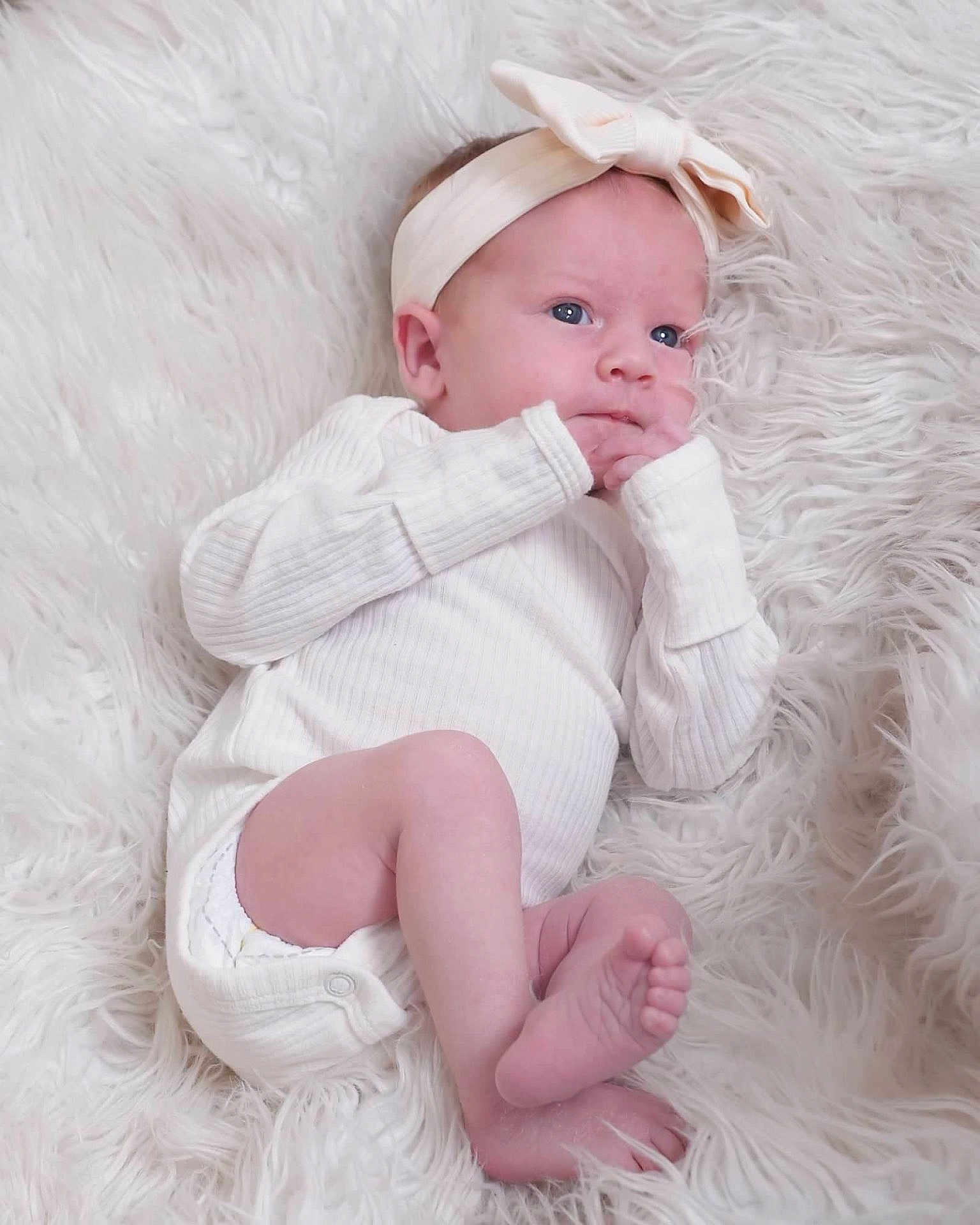 Madelynn joined the competition — help win amazing prizes! baby, infant, newborn, white_clothing, headband, bow, blue_eyes, hand, foot, fingers, lying_down, fluffy_rug, soft_texture, cute, portrait, indoors, cozy, sleepwear, child, person