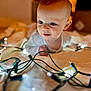 baby, infant, child, face, eyes, blanket, string_lights, glowing, soft_lighting, indoors, cute, curious, portrait, closeup, head, expression, warm_colors, cozy, young, toddler