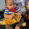 baby, child, potato_chips, snack, table, indoor, fireworks, bandana, striped_shirt, celebration, holiday, food, curious, feet, chubby, bag, red, blue, gray_pants, person