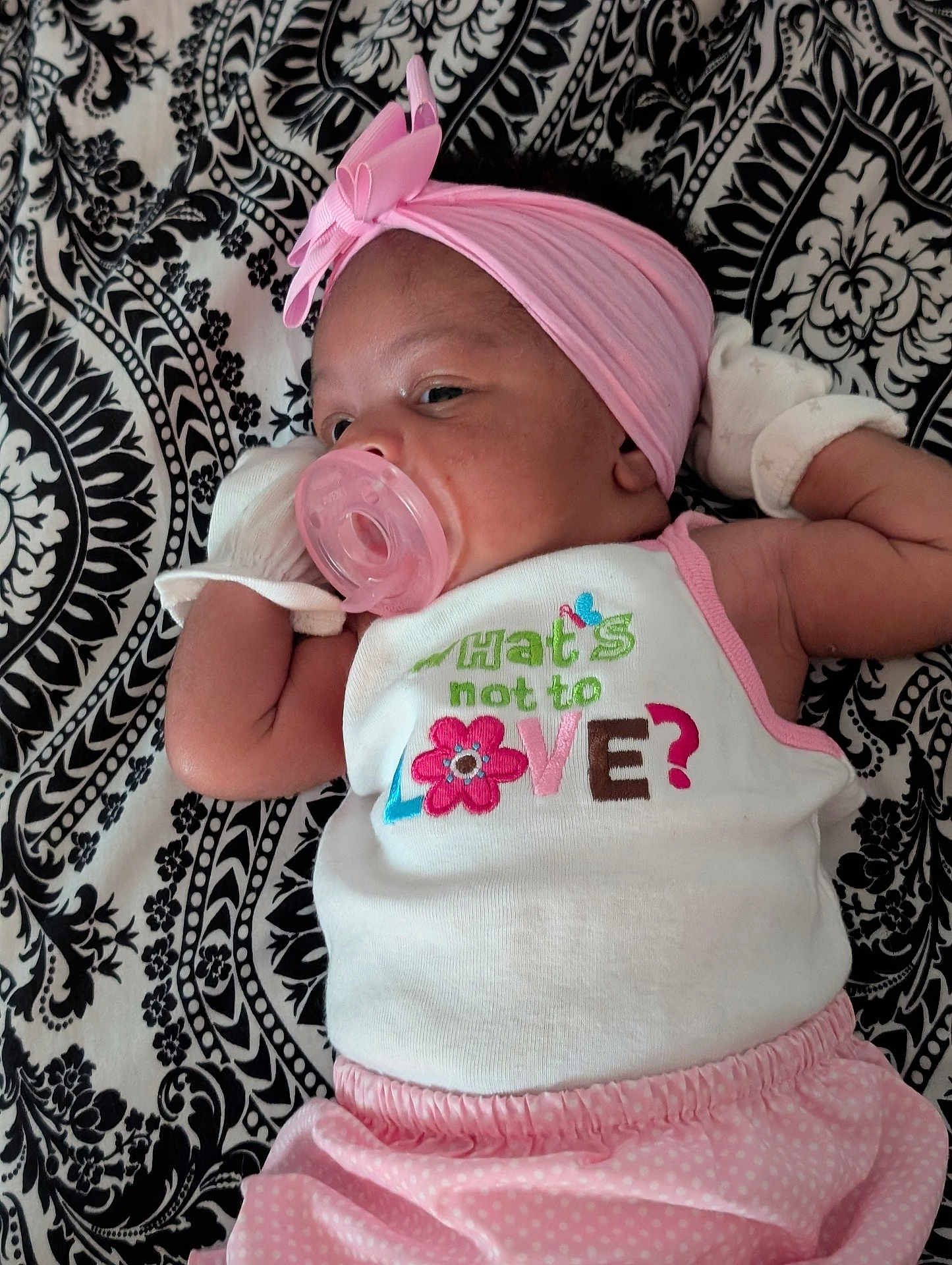 Miracle is registered to the contest to win money with this photo: baby, infant, pacifier, headband, mittens, pink_clothing, white_tank_top, patterned_blanket, lying_down, close_up, cute, sleepy, child, adorable, soft_lighting, portrait, resting, baby_girl, fabric, text_on_clothing