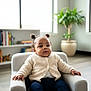 Miracle is registered to the contest to win money with this photo: armchair, baby, bookshelf, child, comfortable, cozy, cute, furniture, home, indoor, infant, knitted_cardigan, natural_light, navy_pants, person, pigtails, plant, portrait, smiling, window