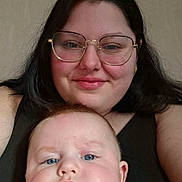 Nathan participe au concours pour gagner de l'argent avec cette photo : adult, baby, baby_onesie, black_hair, blue_eyes, chubby_cheeks, close_up, clothing, face, glasses, glasses_frame, indoor, light_skin, onesie, parent, portrait, selfie, smile, wall_background, woman