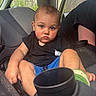 toddler, child, car_seat, vehicle_interior, black_shirt, blue_shorts, seatbelt, car_door, forest_background, serious_expression, short_hair, skin, hand, footwear, car_window, person, indoors, seat, grip, sitting