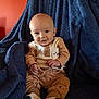 Rowdy is registered to the contest to win money with this photo: baby, child, smiling, sitting, blue_blanket, orange_wall, cozy, cute_clothing, indoor, portrait, happy, infant, face, hands, feet, buttoned_shirt, patterned_pants, warm_lighting, soft_texture, comfortable