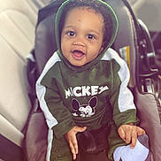 Noah is registered to the contest to win money with this photo: baby, child, car_seat, green_hoodie, mickey_mouse, smiling, happy, indoors, seatbelt, clothing, hood, cute, person, socks, car_interior, portrait, young_child, infant, face, hands