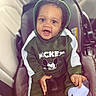baby, child, car_seat, green_hoodie, mickey_mouse, smiling, happy, indoors, seatbelt, clothing, hood, cute, person, socks, car_interior, portrait, young_child, infant, face, hands