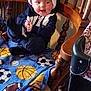 Robert is registered to the contest to win money with this photo: baby, child, infant, clothing, hat, blanket, sports_theme, basketball, soccer_ball, football, chair, wooden_furniture, indoors, happy, smiling, hands_clapping, cozy, seated, person, cute
