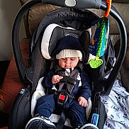 Robert is registered to the contest to win money with this photo: baby, infant, car_seat, child, hoodie, hat, sneakers, toy, seat_belt, black, white, blue, indoor, blanket, panda_pattern, carrying_handle, curious, strapped_in, toddler, cute