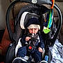 baby, infant, car_seat, child, hoodie, hat, sneakers, toy, seat_belt, black, white, blue, indoor, blanket, panda_pattern, carrying_handle, curious, strapped_in, toddler, cute