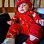 baby, child, hoodie, red_clothing, white_shoes, wooden_chair, indoor, cute, infant, sitting, cozy, patterned_clothing, toddler, comfortable, curious, plush_blanket, portrait, face, small_hands, casual