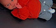 Robert joined the competition — help win amazing prizes! baby, infant, child, orange_sweater, grey_pants, lying_down, black_surface, hand_near_mouth, curious_expression, glowing_hearts, pink_hearts, casual_clothing, cute, small_hands, indoors, portrait, young_child, cozy, resting, love