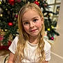 child, girl, blonde_hair, blue_eyes, smile, white_shirt, christmas_tree, holiday_decorations, ornaments, indoor, portrait, festive, happy, cute, young, long_hair, seasonal, celebration, decoration, holiday