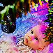 Summer-Rose joined the competition — help win amazing prizes! baby, blanket, christmas_tree, closeup, clothing, colorful_lights, curious, cute, decoration, eyes, face, festive, holiday, holiday_lighting, indoors, infant, ornament, person, portrait, soft_texture