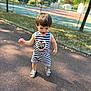 Clément a rejoint le concours — aidez-le/la à gagner de superbes lots ! blue_sandals, casual, child, court, daytime, fence, happy, nature, outdoor, pavement, playful, romper, shadow, striped_clothing, summer, sunlight, toddler, trees, walking, young_child