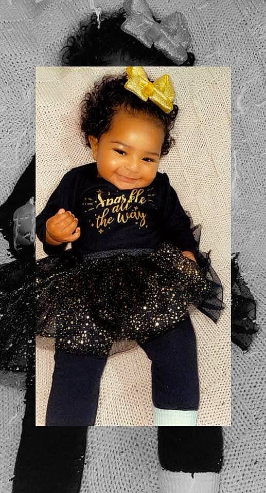 Amya is registered to the contest to win money with this photo: baby, baby_toddler_clothing, chair, dress, embellishment, eye, fashion_design, hairstyle, happy, human_body, iris, joy, knee, neck, pattern, person, sitting, sleeve, standing, thigh