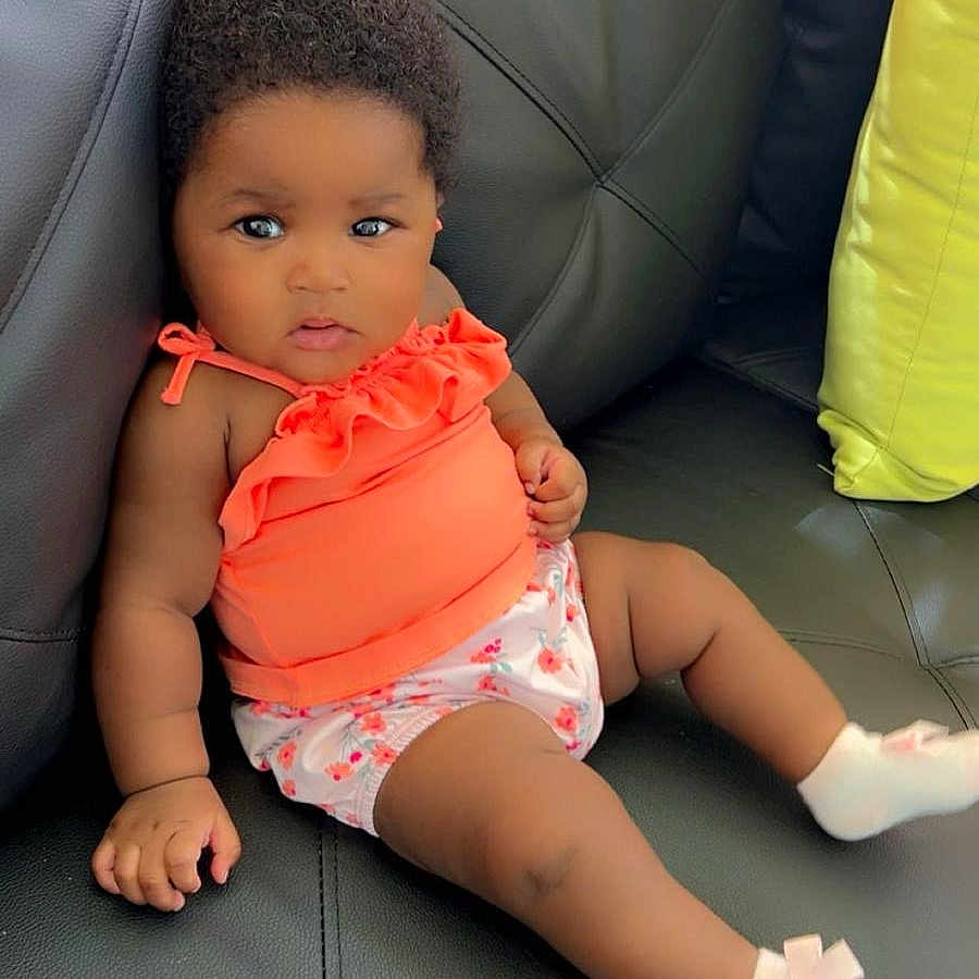 Armony Cara Francis is registered to the contest to win money with this photo: baby, black_leather, child, couch, curious, cute, expression, floral_shorts, furniture, hair, indoor, infant, orange_top, pink_bows, portrait, relaxed, seated, skin, small_hands, socks