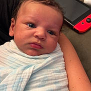 George is registered to the contest to win money with this photo: baby, infant, blanket, swaddle, person, face, arm, indoor, couch, gaming_console, nintendo_switch, pacifier, soft_texture, closeup, resting, curious, child, newborn, casual, home