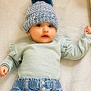 Alyana joined the competition — help win amazing prizes! baby, infant, hat, knitted_hat, pom_pom, sweater, ruffles, denim_pants, clothing, blanket, soft_texture, lying_down, cute, face, portrait, child, young, indoor, warm, expression