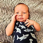 Sawyer is registered to the contest to win money with this photo: baby, infant, child, face, hand, onesie, clothing, shark_pattern, blanket, texture, lying_down, curious, expression, skin, head, portrait, young_child, indoors, person, cute