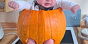 Ethan is registered to the contest to win money with this photo: baby, pumpkin, hat, legs, arms, face, expression, kitchen, stove, countertop, orange, green, white_clothing, infant, cute, holiday, festive, indoors, child, costume