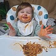 Ethan joined the competition — help win amazing prizes! baby, bib, child, clothing, expression, face, food, fun, hair, hands, happy, high_chair, indoor, meal, messy, plate, smiling, spaghetti, table, toddler