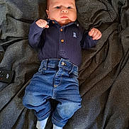 Ethan is registered to the contest to win money with this photo: baby, infant, child, denim_jeans, navy_shirt, socks, blanket, remote_control, fist, cute, lying_down, portrait, clothing, indoor, person, toddler, fabric, soft, casual_wear, cozy