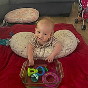 Charles joined the competition — help win amazing prizes! baby, infant, smiling, pillow, red_blanket, toys, glass_dish, living_room, couch, wooden_floor, child, play, floor, stroller, patterned_pillow, happy, indoor, person, colorful, young_child