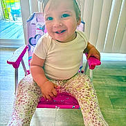 Ainoha is registered to the contest to win money with this photo: baby, child, smiling, sitting, chair, headband, bow, white_shirt, floral_leggings, indoor, flooring, natural_light, window, blinds, pink, purple, cute, happy, person, toddler
