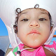 Zoey joined the competition — help win amazing prizes! child, face, hat, sunhat, pink_clothing, curly_hair, outdoor, blue_sky, person, closeup, portrait, summer, vacation, lounge_chair, sunlight, young_child, casual, relaxation, daytime, expression