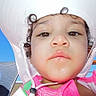 child, face, hat, sunhat, pink_clothing, curly_hair, outdoor, blue_sky, person, closeup, portrait, summer, vacation, lounge_chair, sunlight, young_child, casual, relaxation, daytime, expression