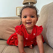 Mïa participe au concours pour gagner de l'argent avec cette photo : baby, child, crawling, red_dress, smiling, happy, indoor, couch, pillow, lamp, curly_hair, person, skin, furniture, home, cute, young, portrait, infant, bright