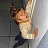 toddler, child, curious, barefoot, striped_shirt, pony_tail, indoor, hallway, tile_floor, wall, young_child, reaching, exploring, person, casual_clothing, small_hands, standing, cute, playful, home