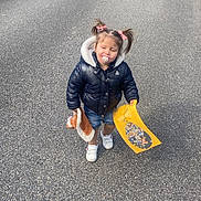 Lyanna participe au concours pour gagner de l'argent avec cette photo : toddler, child, pigtails, pacifier, plush_toy, paper_craft, jacket, shorts, sneakers, street, sidewalk, daylight, outdoor, smiling, happy, asphalt, greenery, fence, graffiti, person
