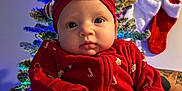 Remi is registered to the contest to win money with this photo: baby, infant, christmas_tree, holiday, red_clothing, headband, bow, stockings, decorations, lights, festive, cute, indoors, person, child, celebration, winter, smile, face, cozy