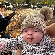 Remi joined the competition — help win amazing prizes! baby, child, hat, pom_poms, knitwear, outdoor, fall, leaves, stroller, hand, cute, tongue_out, person, face, cheeks, clothing, pattern, animal_print, nature, daylight